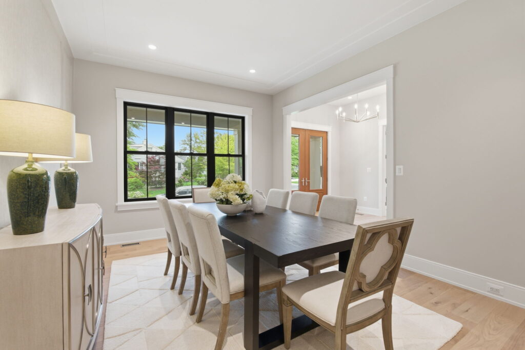 Modern dining room featuring a dark wood table, light upholstered chairs, and a large black-framed window.