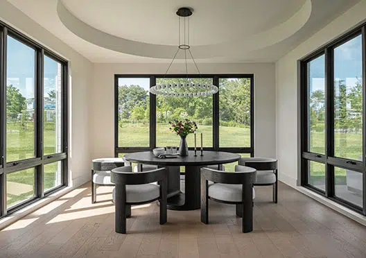 A morning room of white walls and black windows with a circular tray ceiling and round chandelier. A black table and chairs in the center.