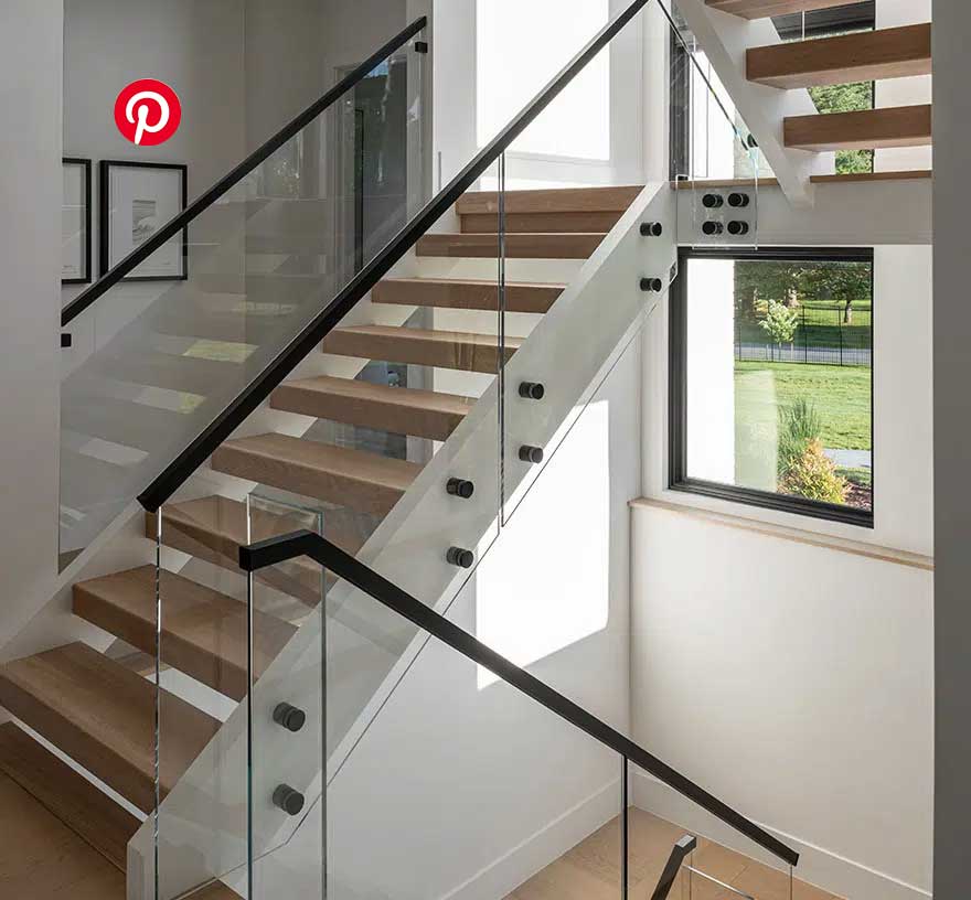 A side view of an open riser staircase with glass walls, black handrails and stained steps. Dark framed windows line the entire staircase.