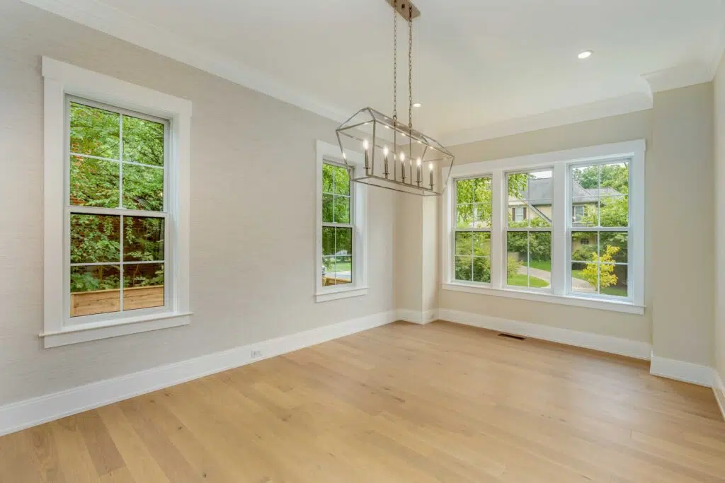 A dining room featuring light wood floors, textured beige wallpaper, white crown molding, large windows, and a hanging polished chrome lantern chandelier.