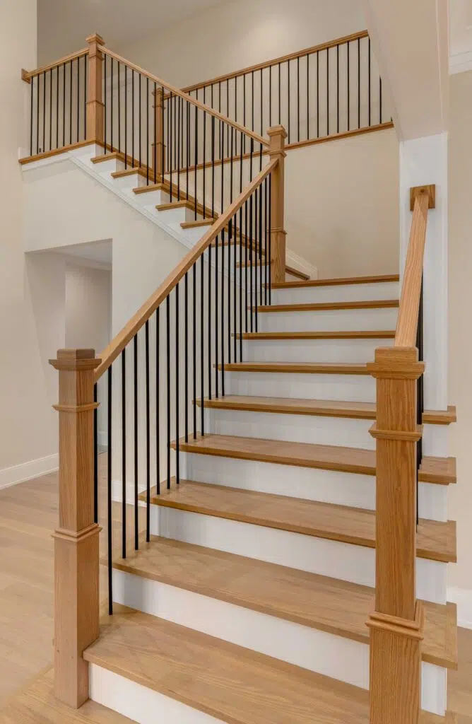 A multi-landing staircase featuring light natural wood treads, white risers, square wood newel posts, matching handrails, and slender black metal balusters.