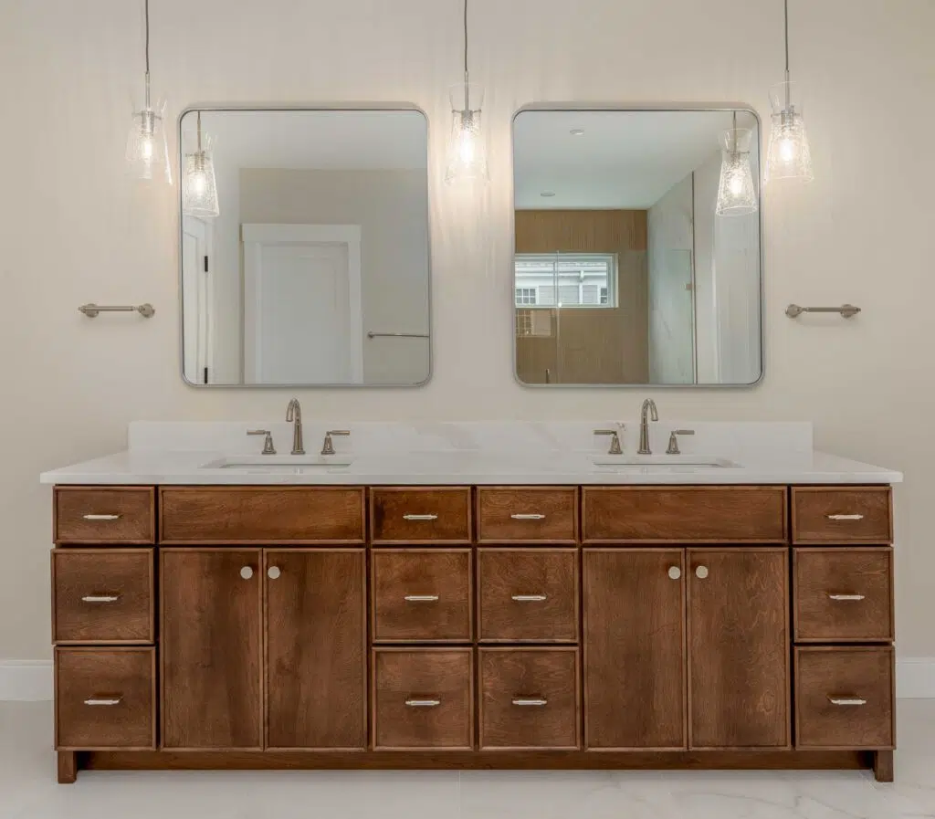 A double bathroom vanity featuring rich stained wood cabinets, a white marble countertop with dual undermount sinks, rounded square mirrors, and three hanging glass pendant lights.