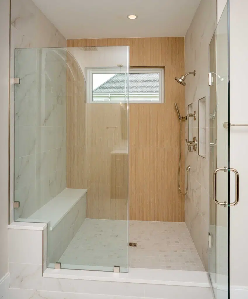A modern walk-in shower with frameless glass enclosures, a built-in bench, marble-look wall tile, a vertical wood-look tile accent wall, and nickel fixtures.