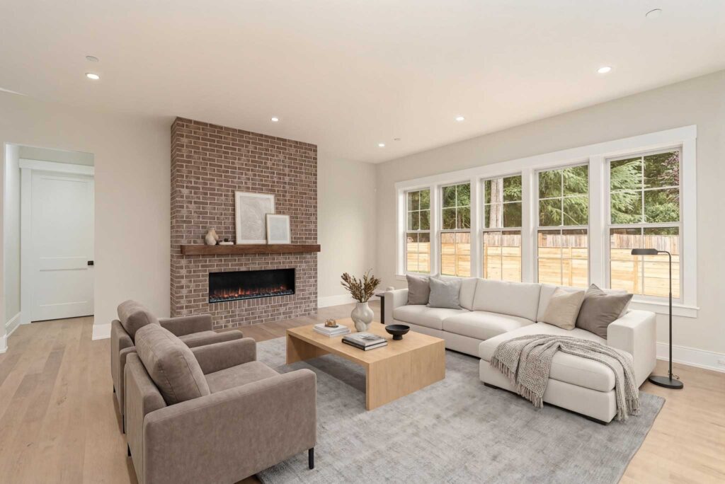 A bright family room with light hardwood floors, a large bank of windows, and a floor-to-ceiling brick accent wall with a dark wood mantel and a linear fireplace insert.